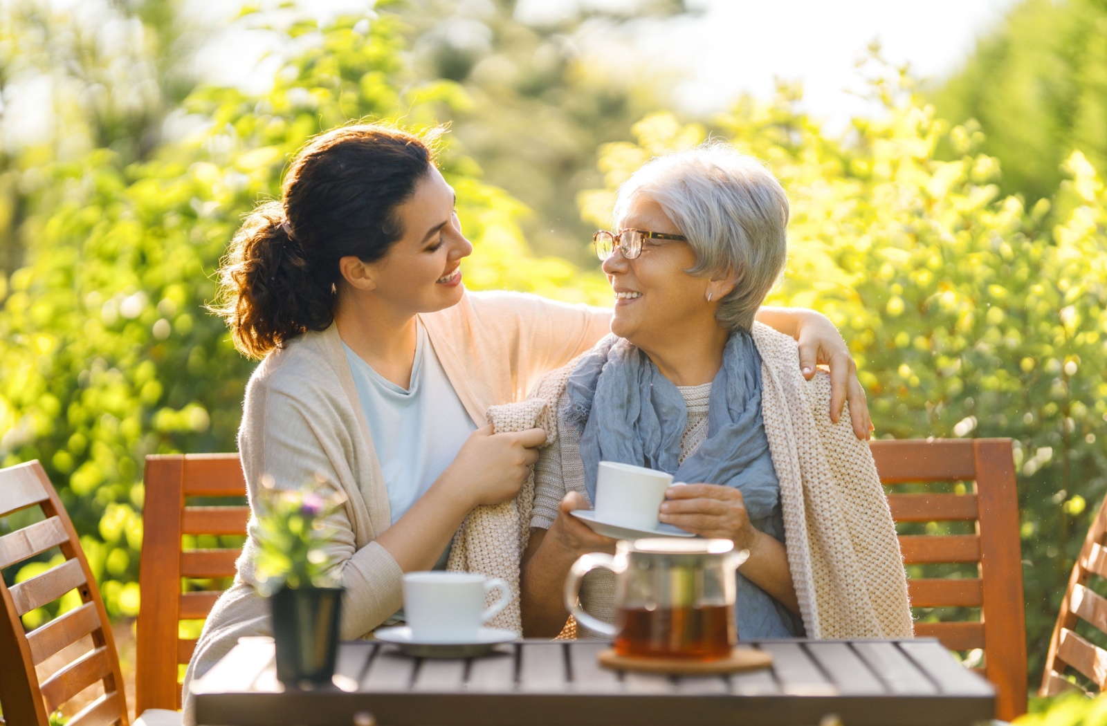 A woman sitting with her mother outside, sharing a cup of tea.