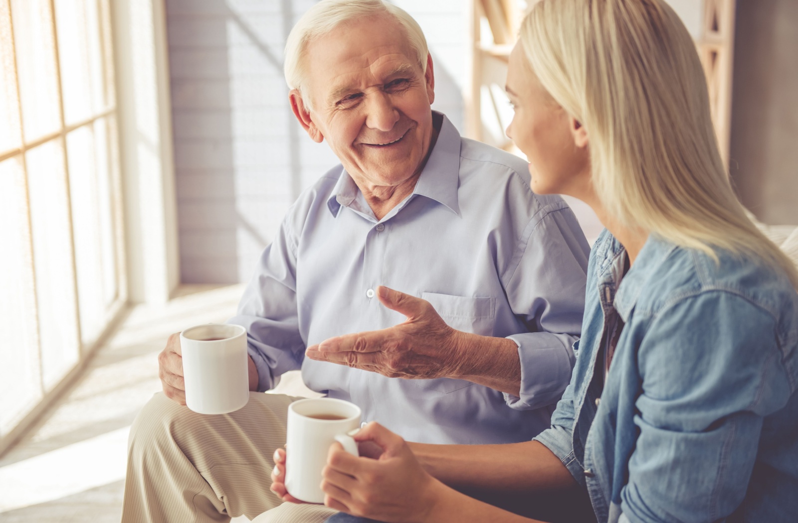 An adult child drinks a mug of coffee and discusses memory care with their senior parent.