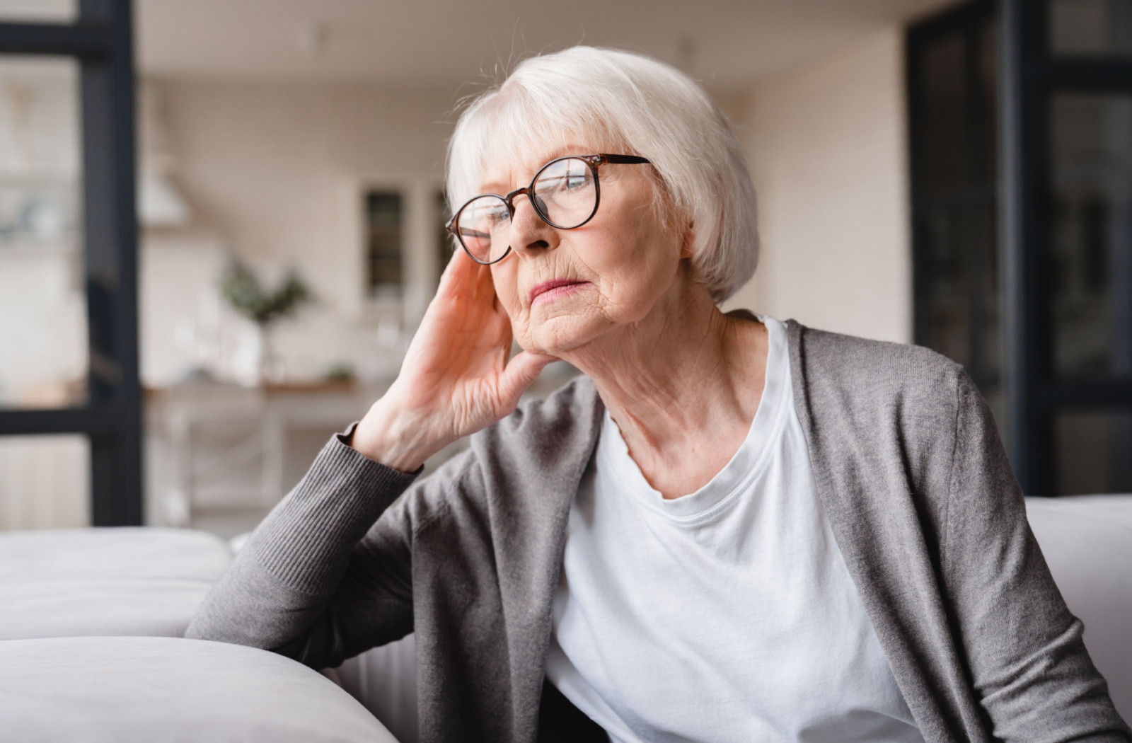 A melancholic senior with early signs of dementia sits alone in their home.