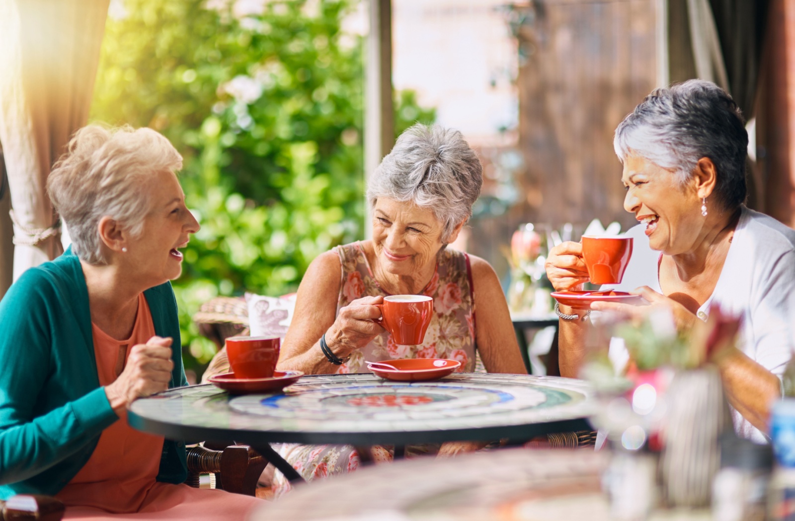 Three senior woman drinking tea and laughing together in a dining area of senior living, enjoying the benefits of social activity.