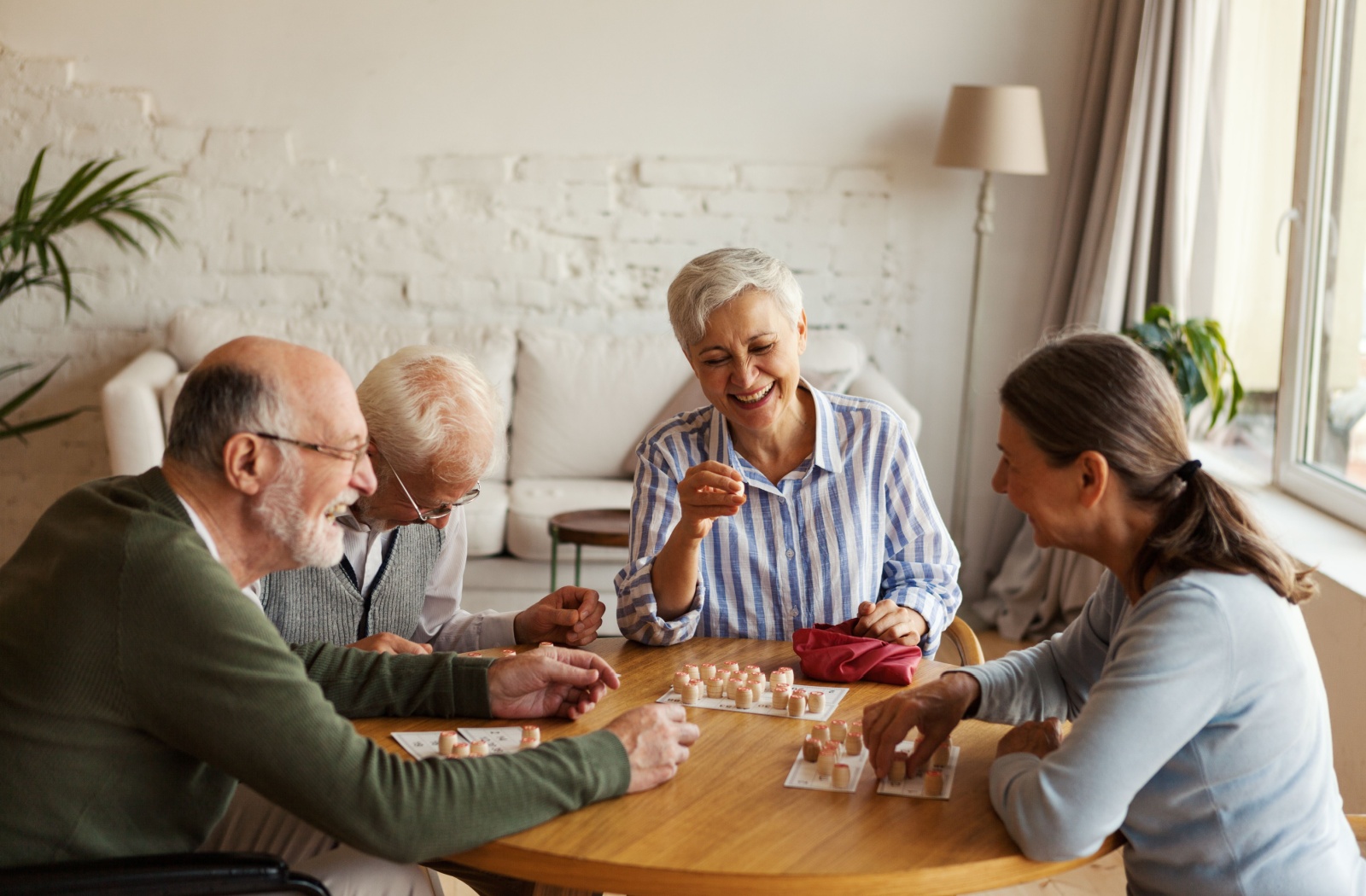 4 seniors in a common area socializing and laughing together while reading a card for a board game.
