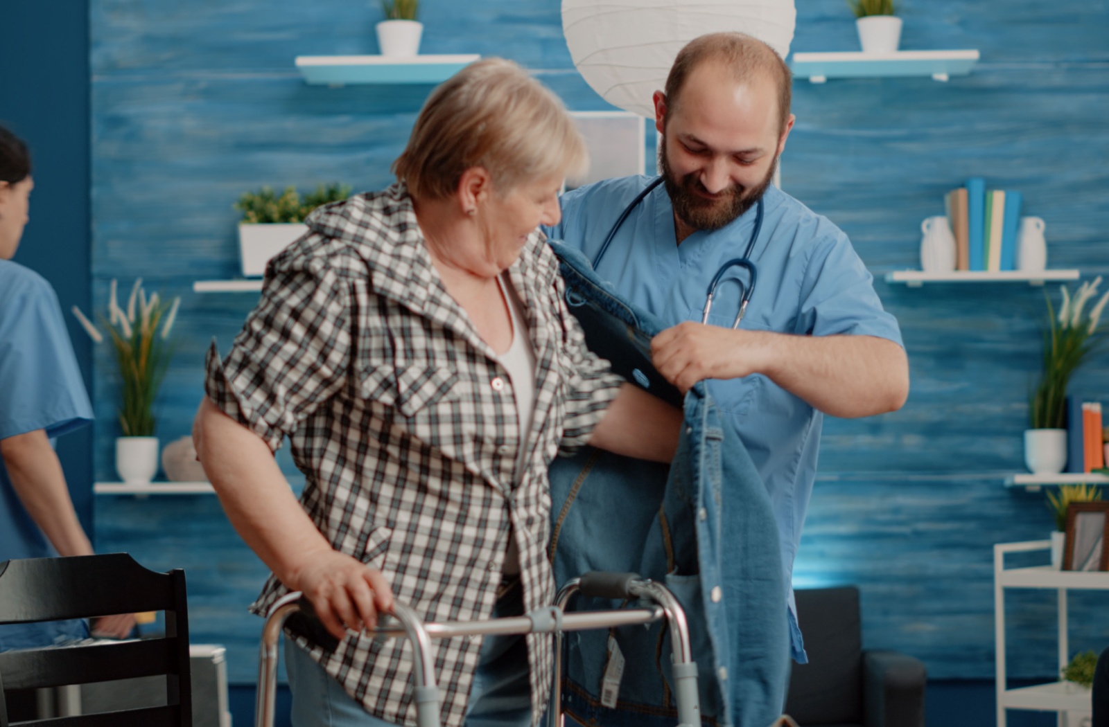 A nurse at a short-term care community helping a senior woman with putting her jacket on.