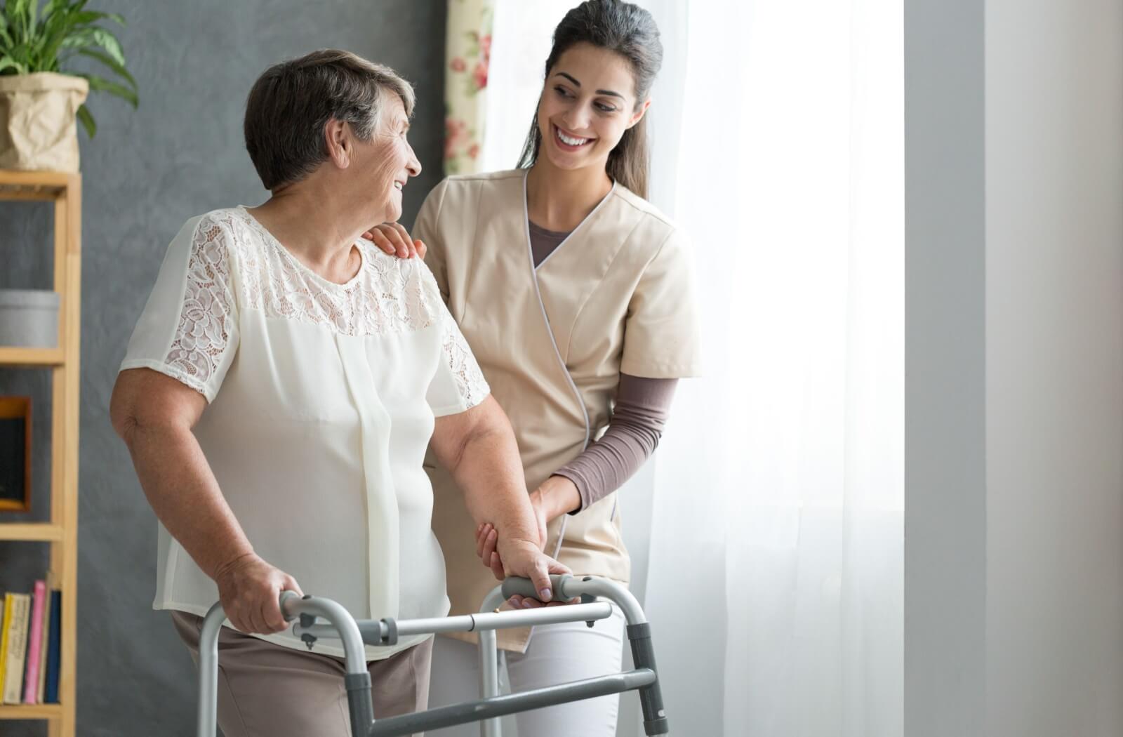 A smiling nurse helping a senior to walk around a nursing home.