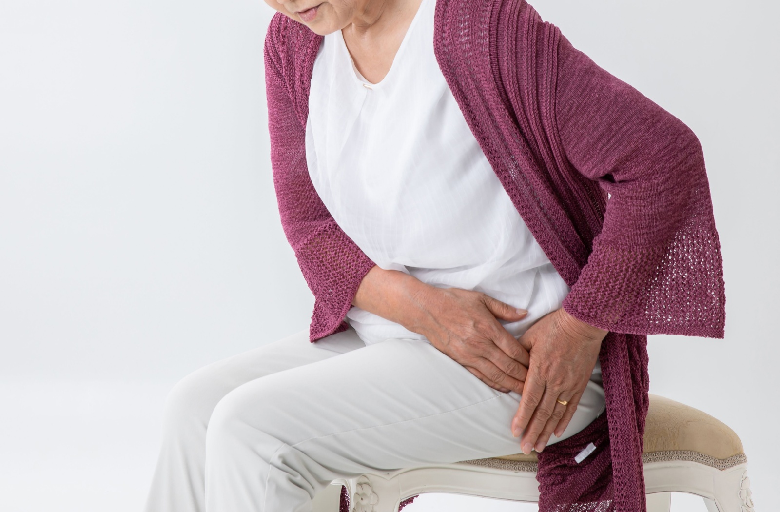 An elderly person holding their hip in pain as they are standing up out of a chair.