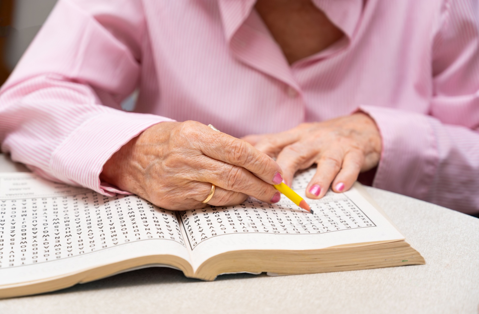 An older adult in a pink shirt does a word search at their kitchen table