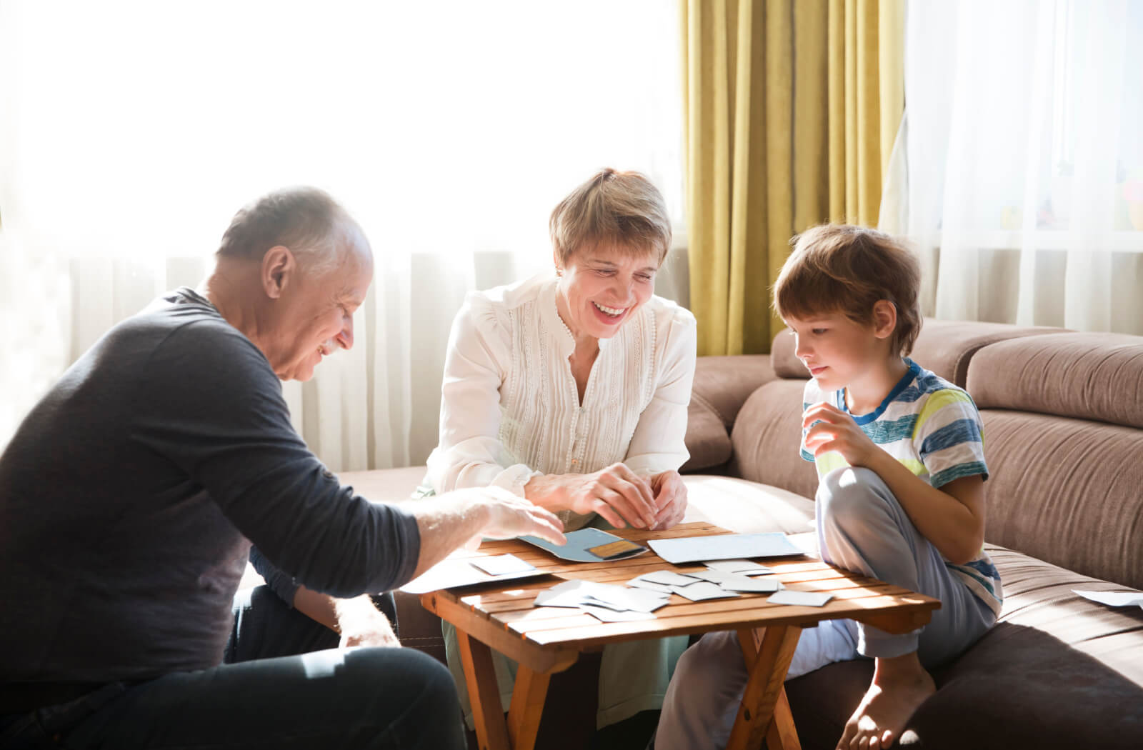 2 older adults playing a word-based card game with their grandchild in their living room