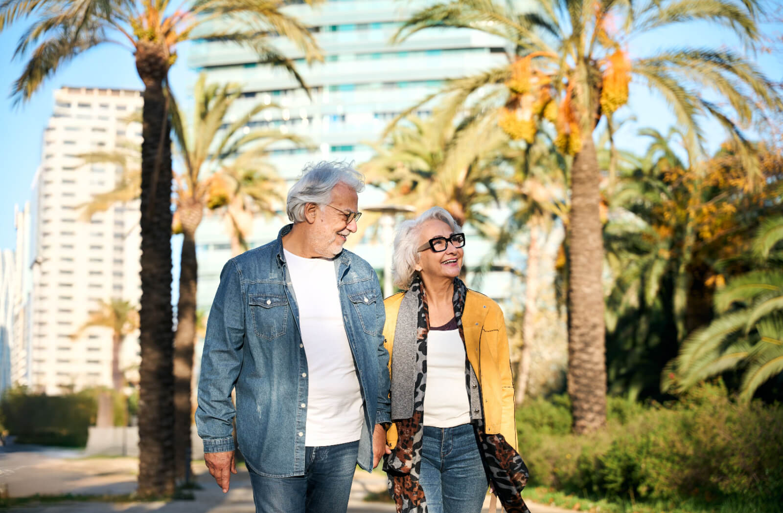 An older married couple walking hand-in-hand along a walking trail lined with trees near Fort Wayne