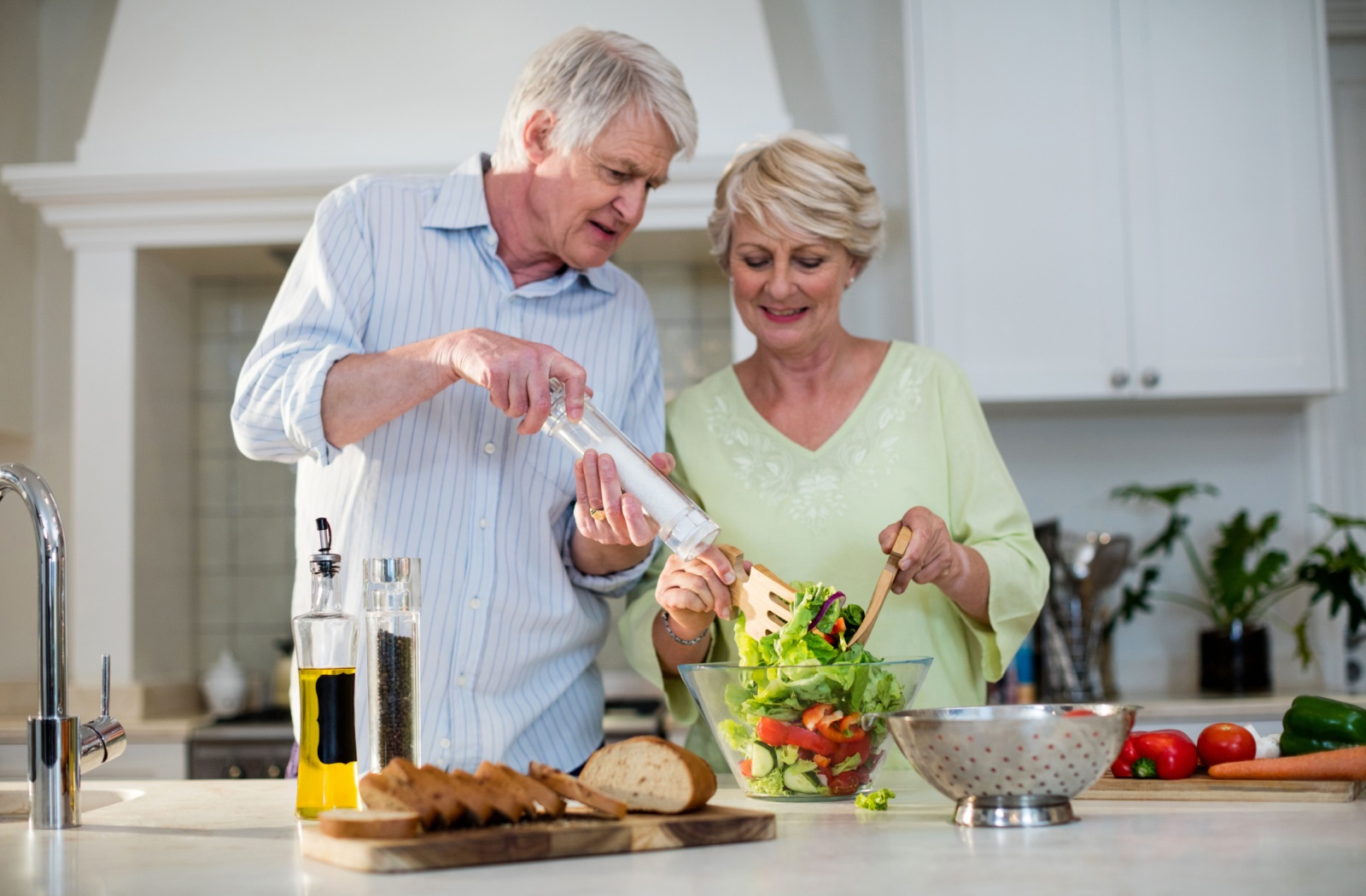 Older adults preparing a healthy snack with fresh salad with lettuce peppers cucumbers and bread on the counter