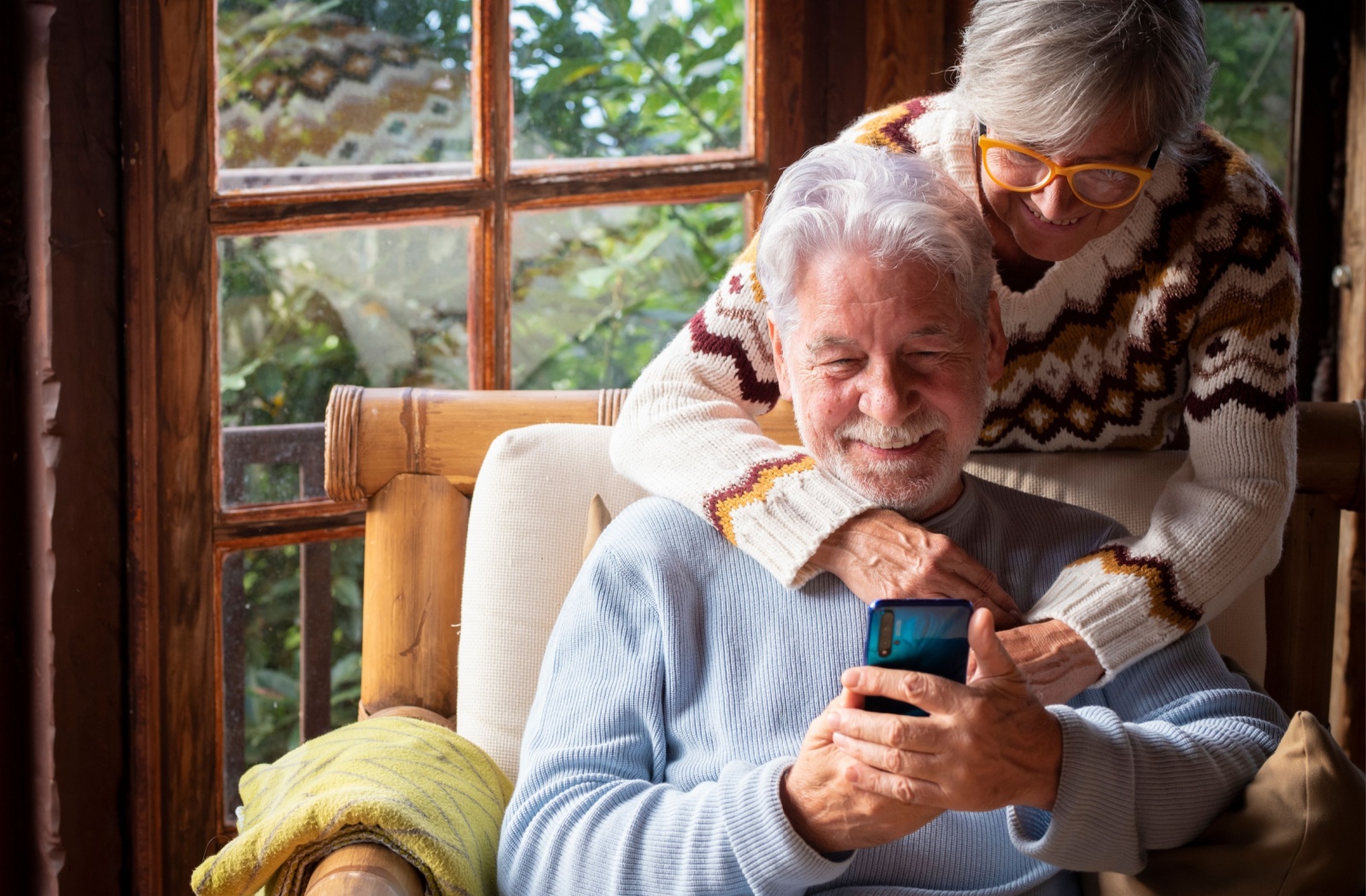 A senior couple watch a video on a smartphone while wearing cozy winter sweaters.