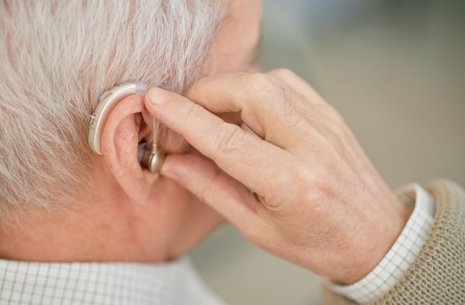 Close up of a senior adjusting their hearing aid in their ear.