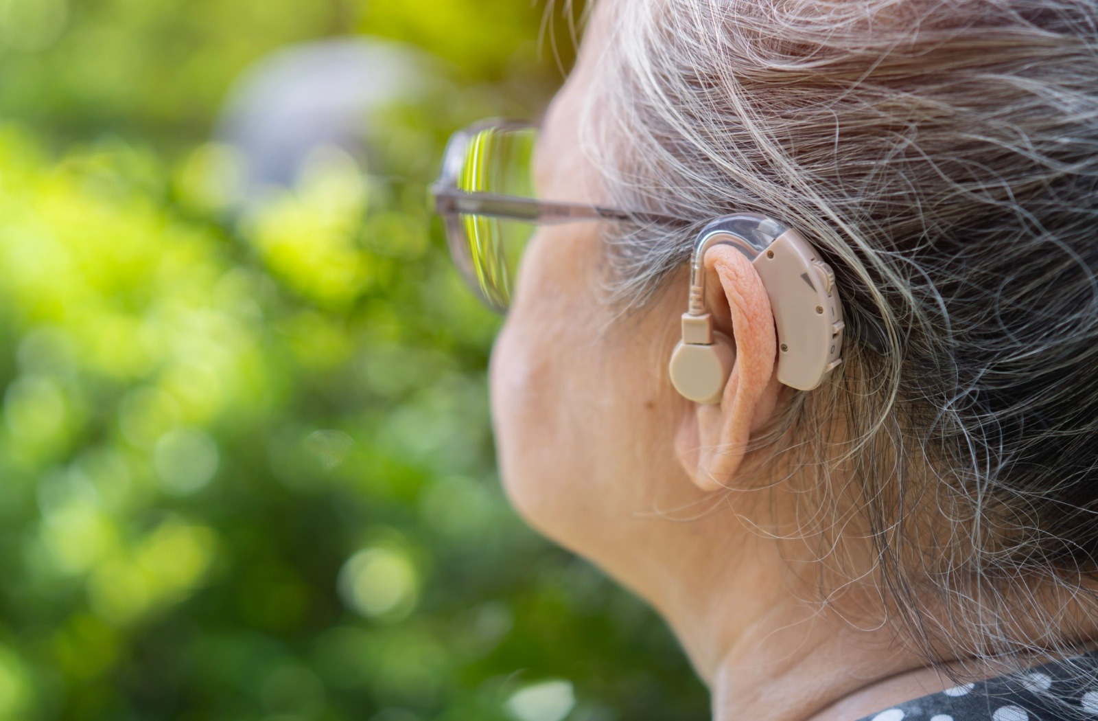 Close up of a senior resident wearing their over-the-ear hearing aid.

